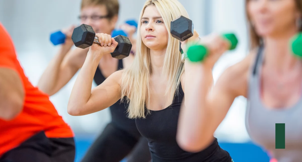 Kobiety z hantlami w dłoniach, robią przysiad. Grupa fitness./ Canva