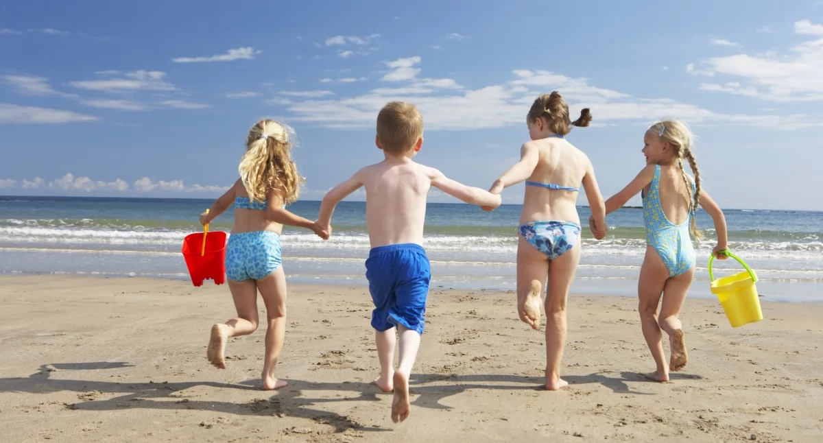 Na zdjęciu: Dzieci biegnące po plaży i trzymające się za ręce. / Canva